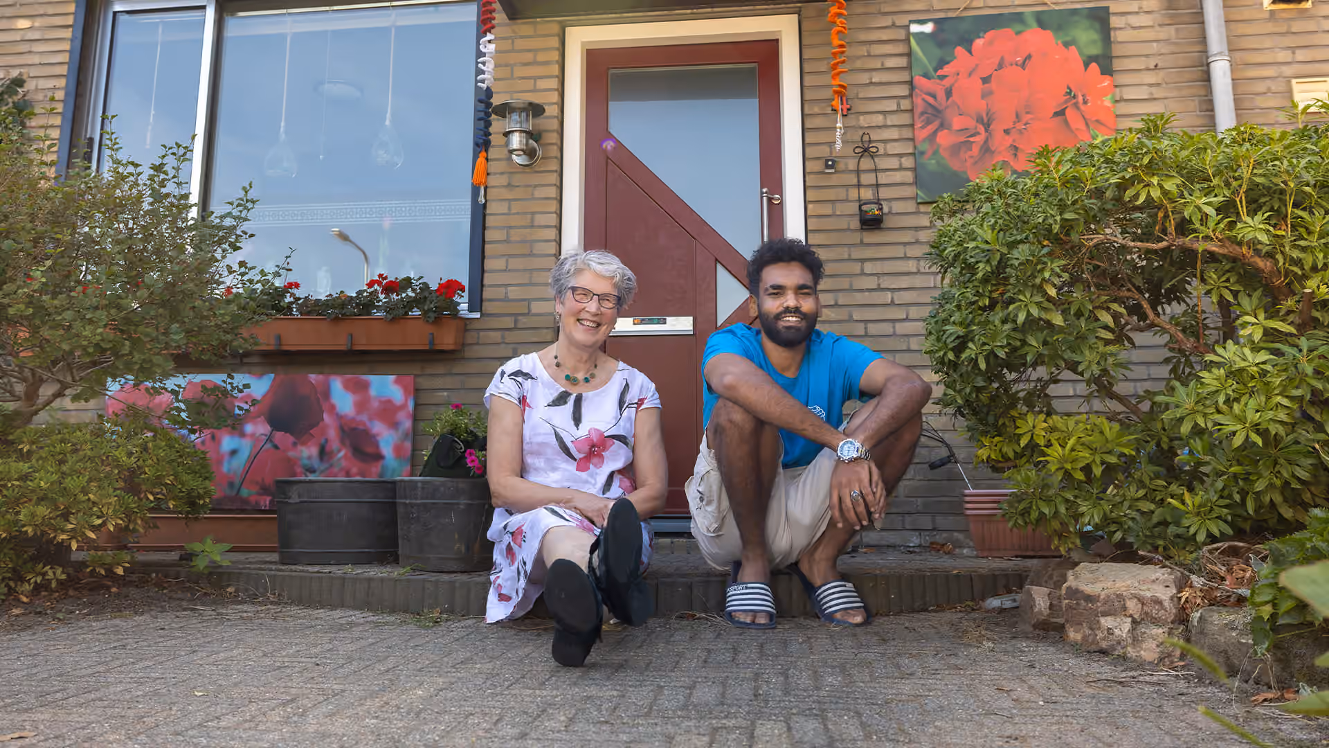 Beeld van Nederlandse gastvrouw Alice en Soedenese vluchteling Lufti voor hun huis